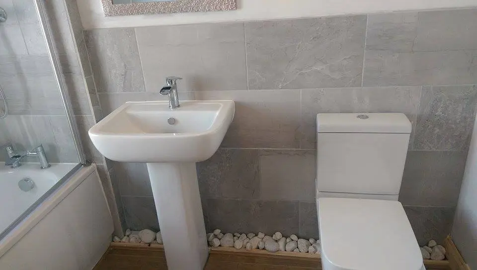 Refitted bathroom with a shower, pedestal basin and toilet against grey tiled walls