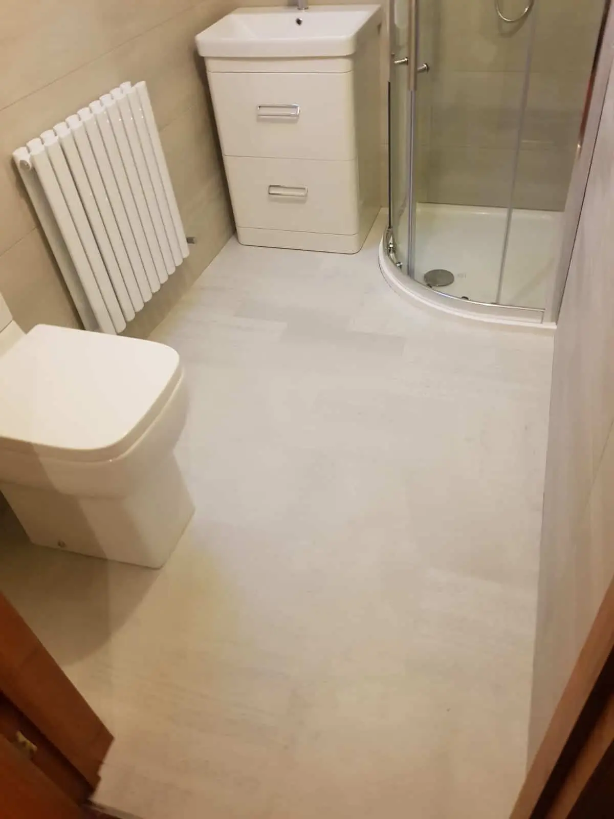 Newly tiled bathroom with a toilet, vanity unit, radiator and curved glass shower enclosure