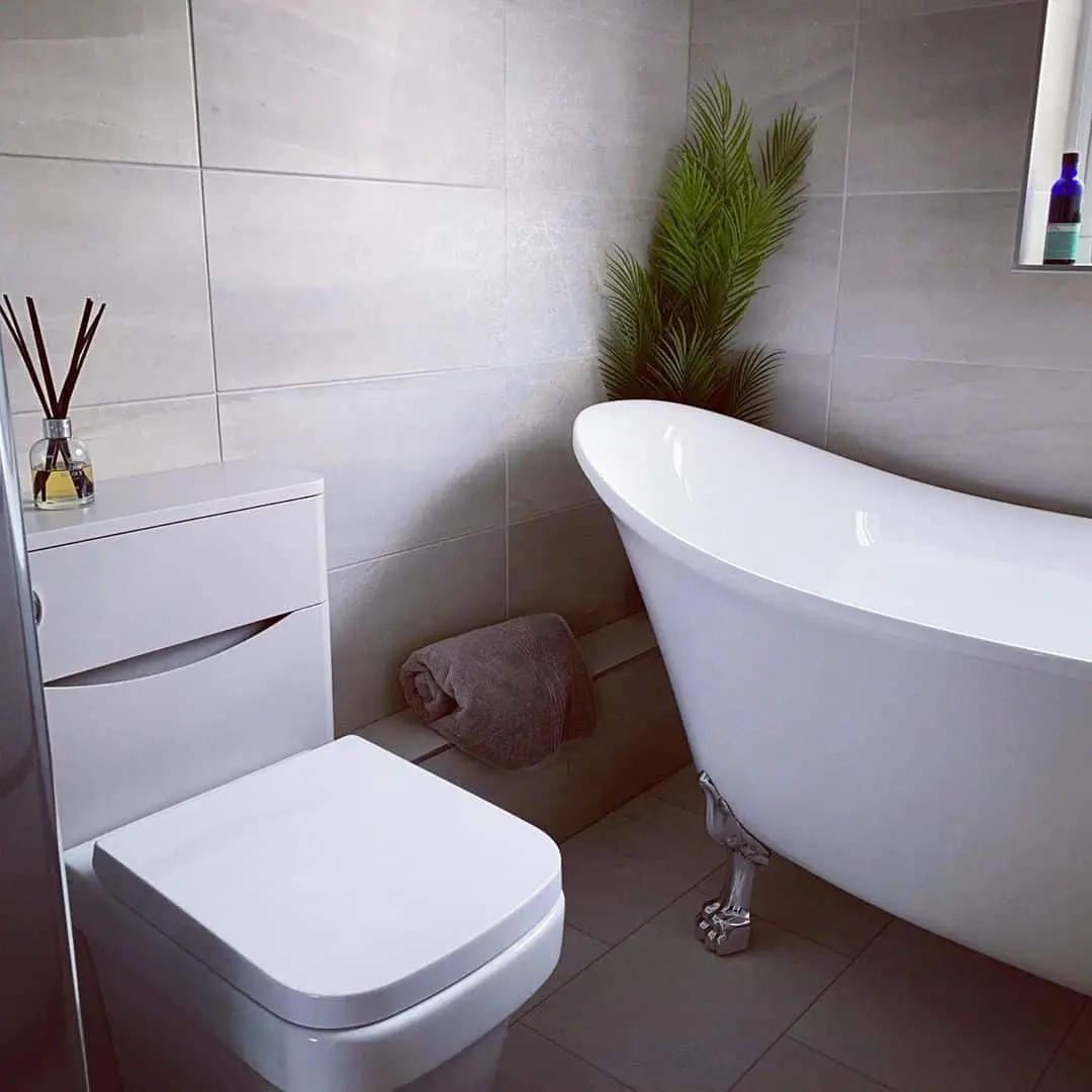 Modern bathroom with a freestanding bath, wall-hung toilet and grey tiled walls.