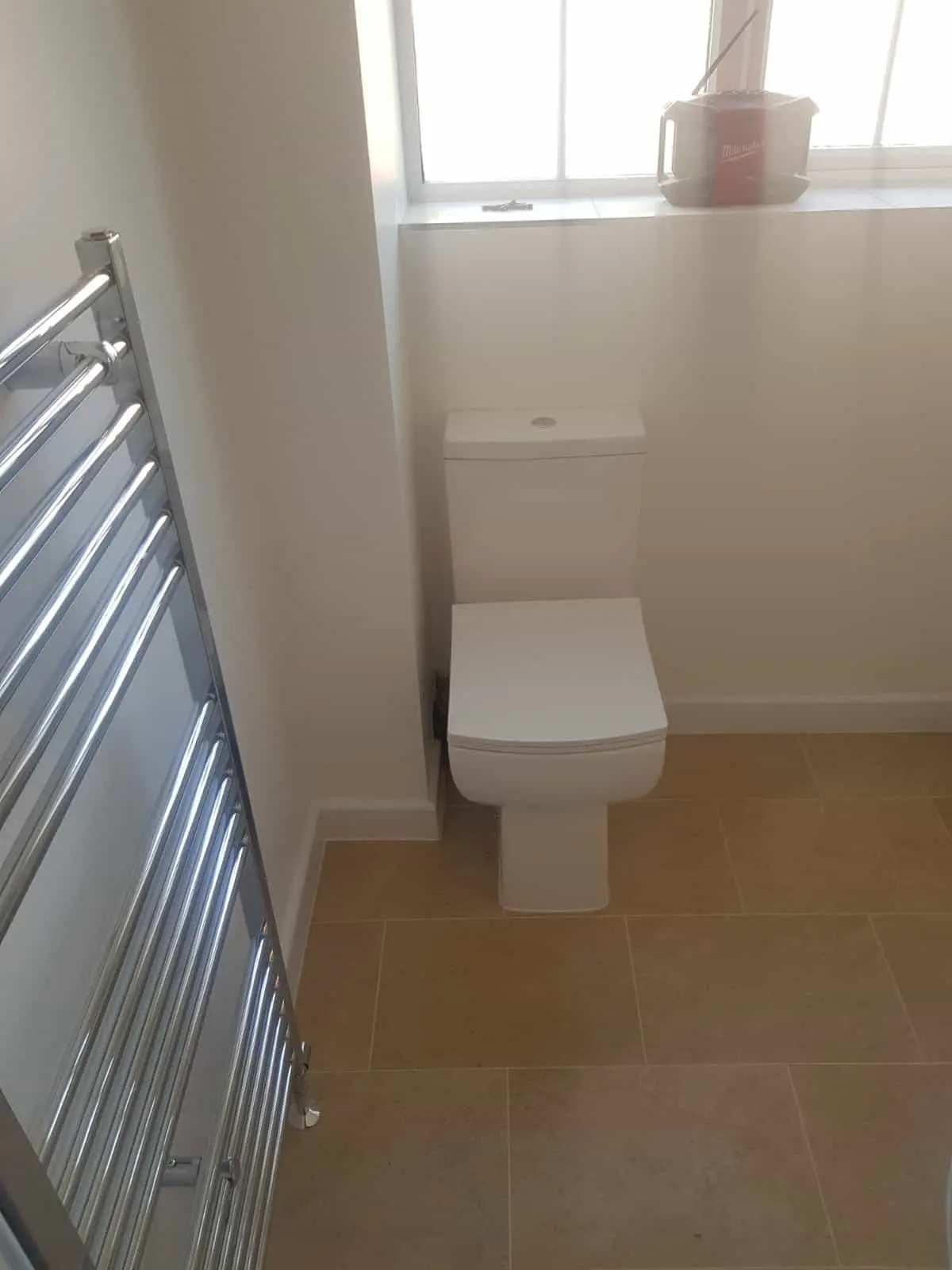 White toilet beside a chrome heated towel rail in a tiled bathroom