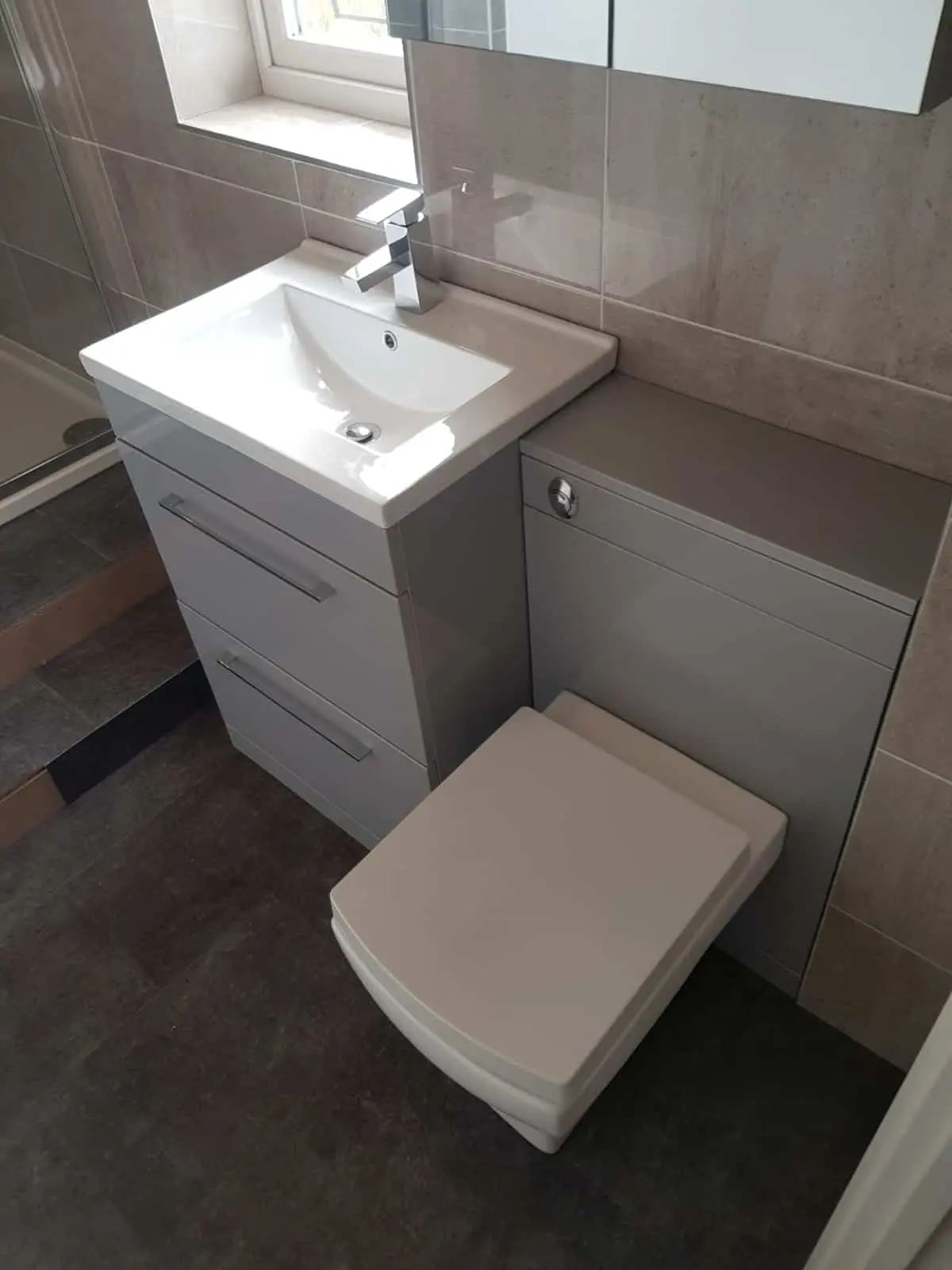 Modern bathroom with a white basin vanity, wall-mounted toilet and grey tiled walls