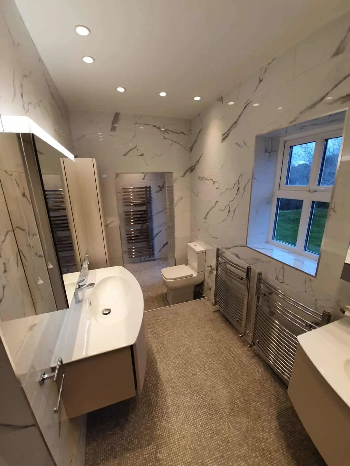 Finished bathroom with marble-effect wall tiles, a vanity basin, toilet and heated towel rails.