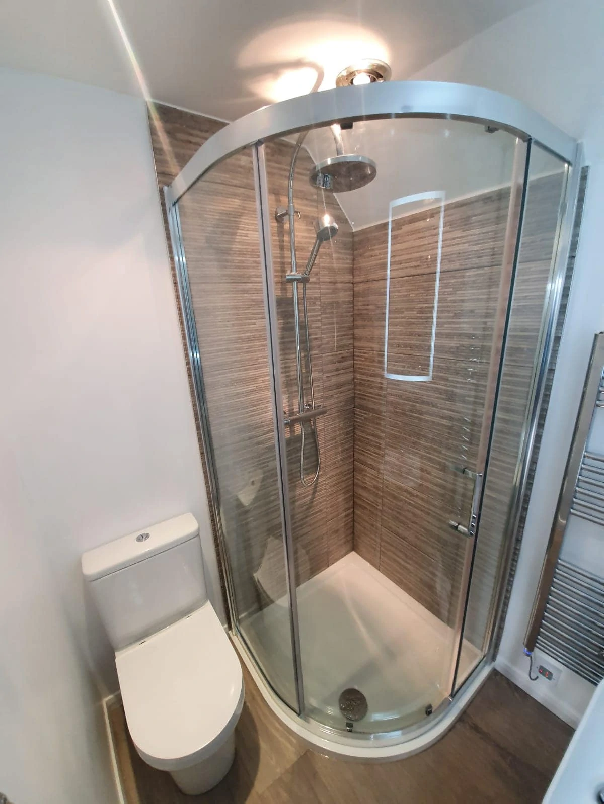 Curved glass shower enclosure beside a white toilet in a tiled bathroom