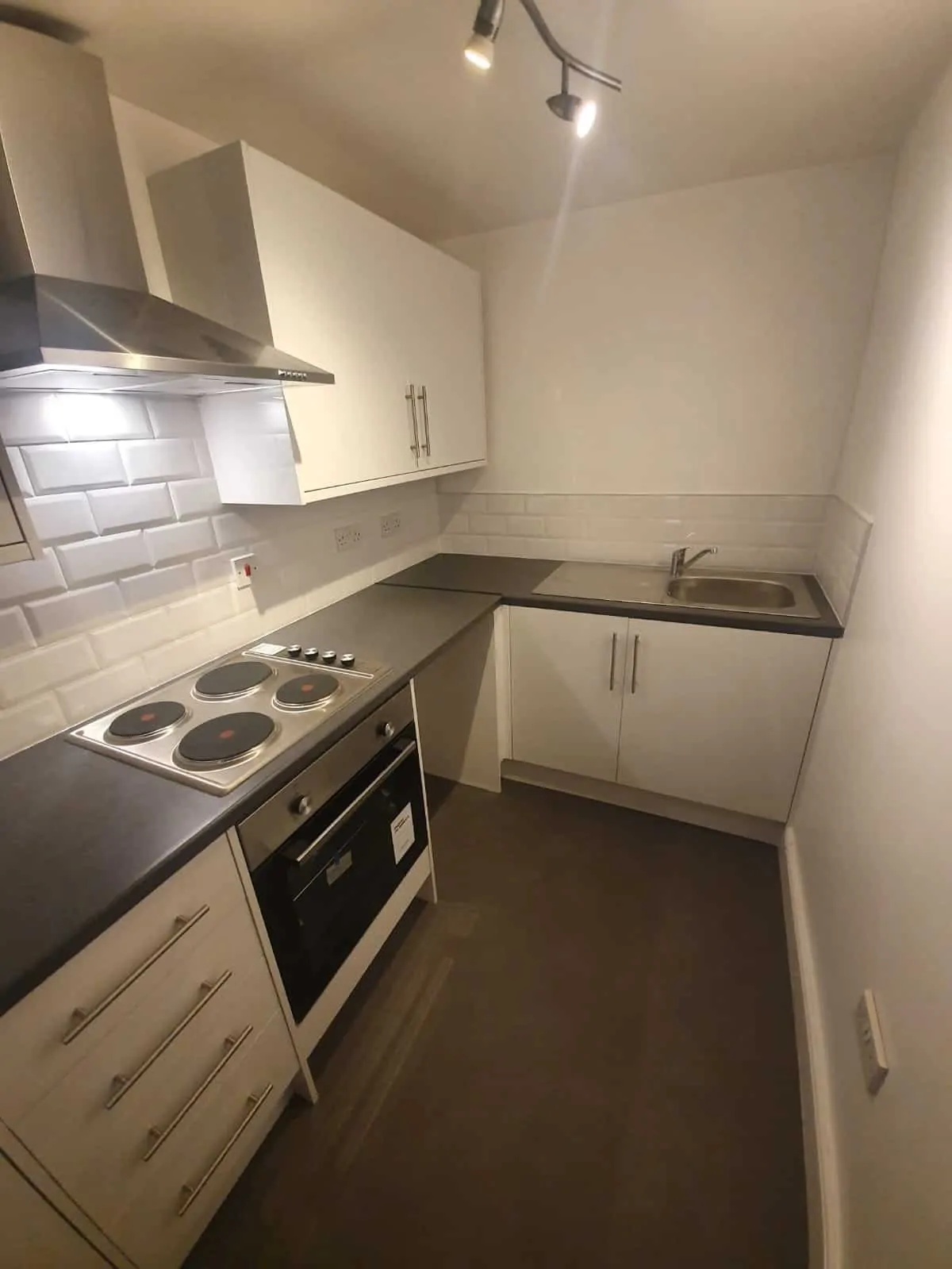 Compact fitted kitchen with cream cabinets, dark worktops, a ceramic hob and built-in oven.