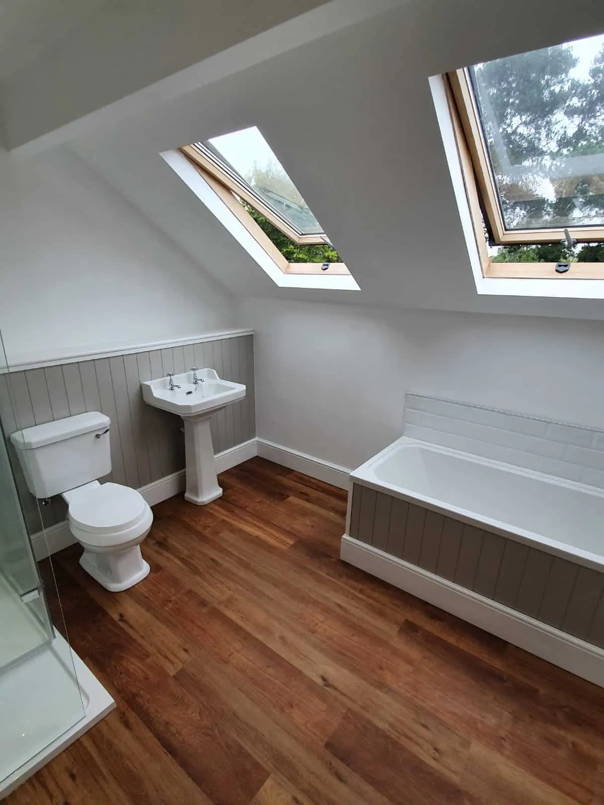 Finished attic bathroom with a bath, shower, toilet, pedestal basin and two roof windows.
