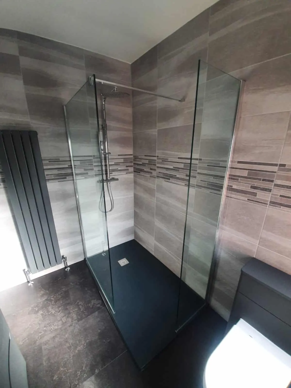 Walk-in shower with glass screens, tiled walls and dark flooring