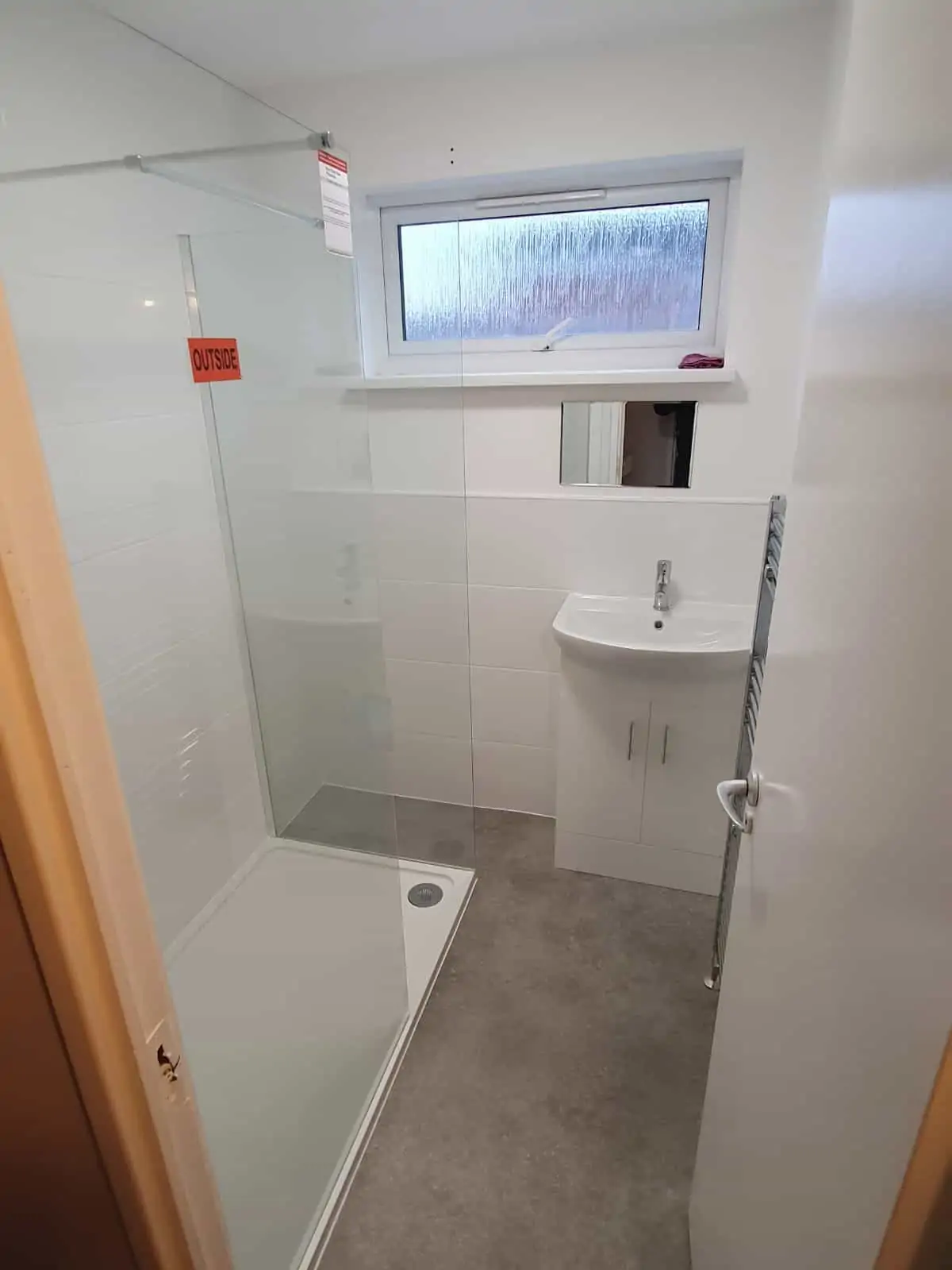 Compact bathroom with a glass shower enclosure, vanity basin and tiled walls