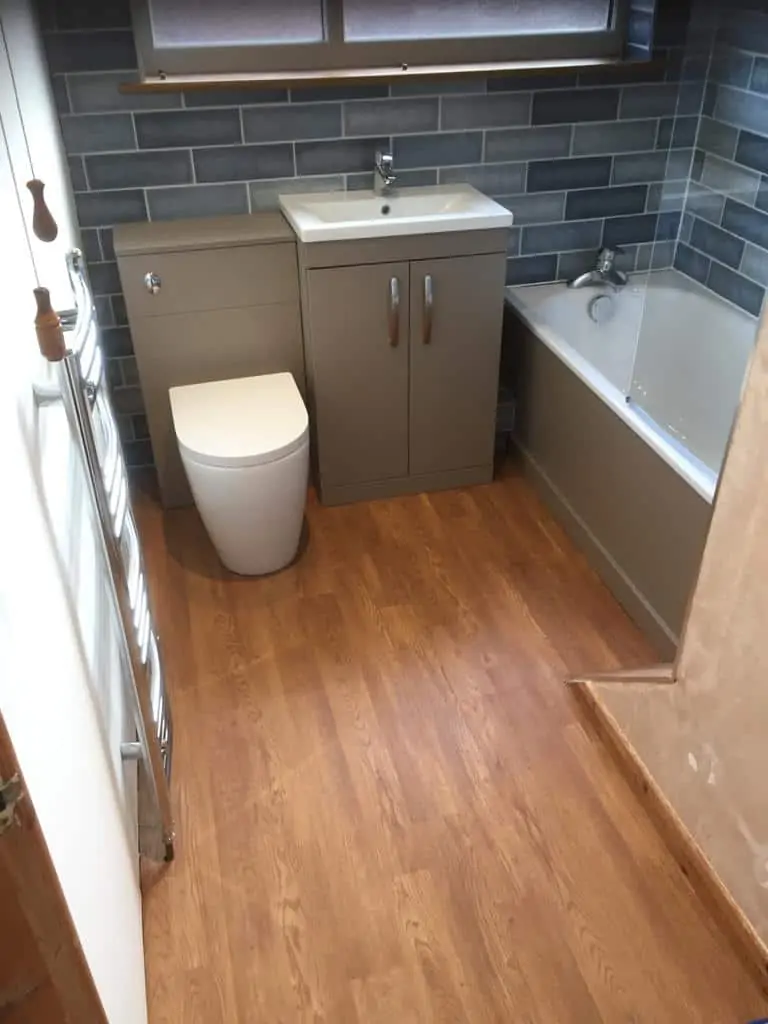 Bathroom with a bath, toilet, vanity basin, grey tiled walls and wood-effect flooring