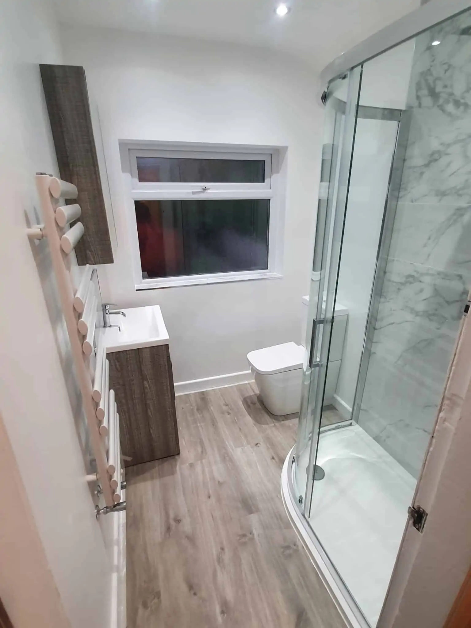Refurbished bathroom with a glass shower enclosure, wall-mounted basin, toilet and wood-effect flooring