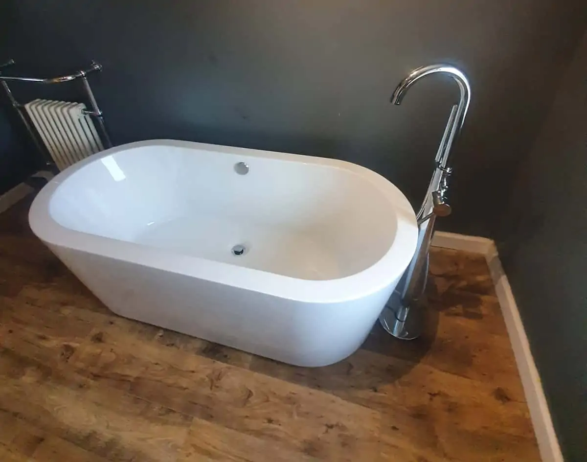 White freestanding bath with a chrome floor-mounted tap on an oak-effect floor