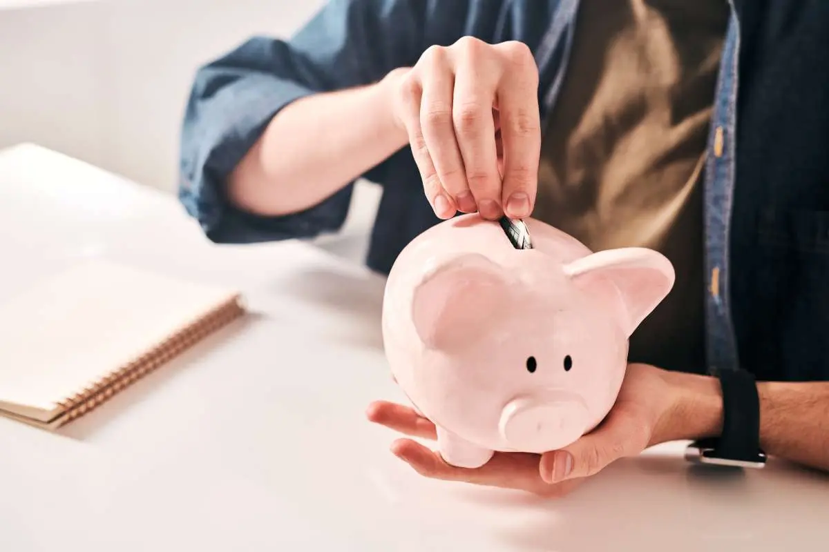 A person putting a coin into a pink piggy bank