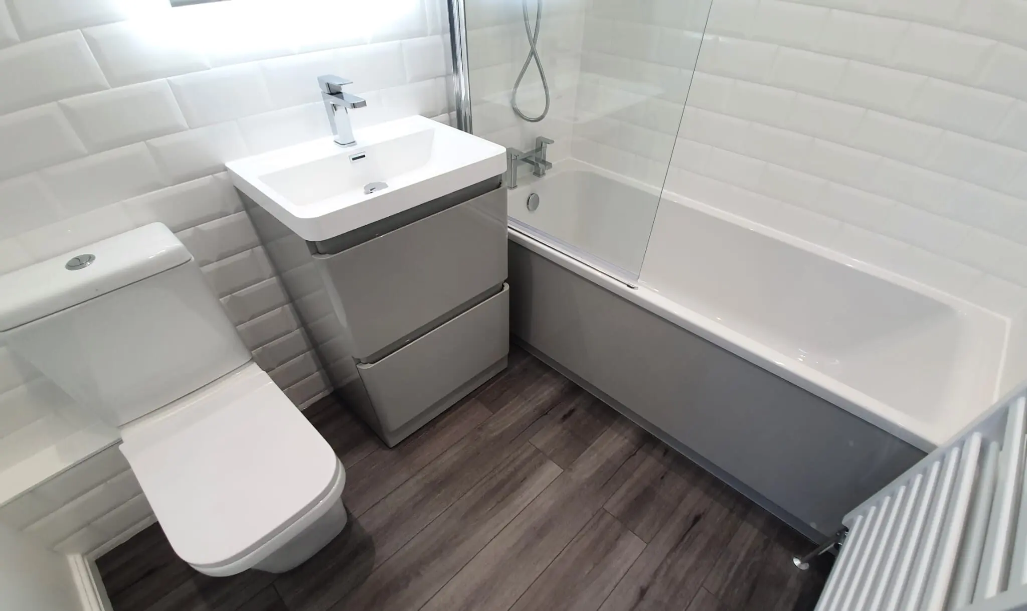 Renovated bathroom with a toilet, vanity basin, bath and tiled walls