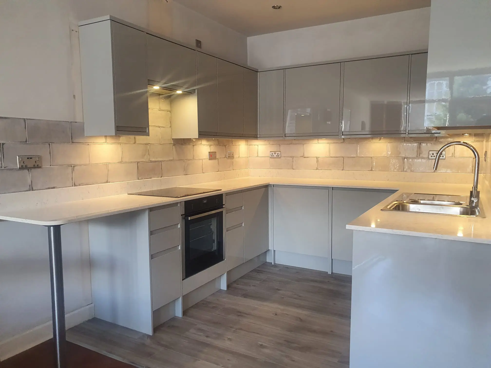 Modern light grey kitchen with white worktops, tiled splashback and built-in oven