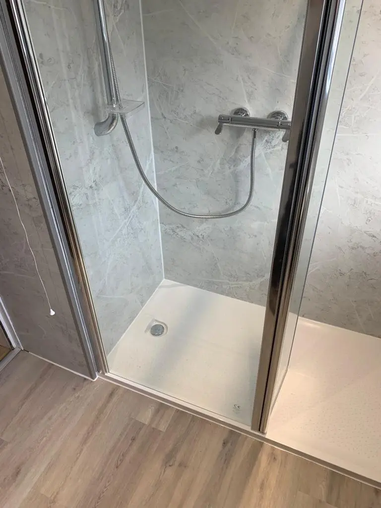 Walk-in shower with a low white tray, glass enclosure and grey marble-effect tiles