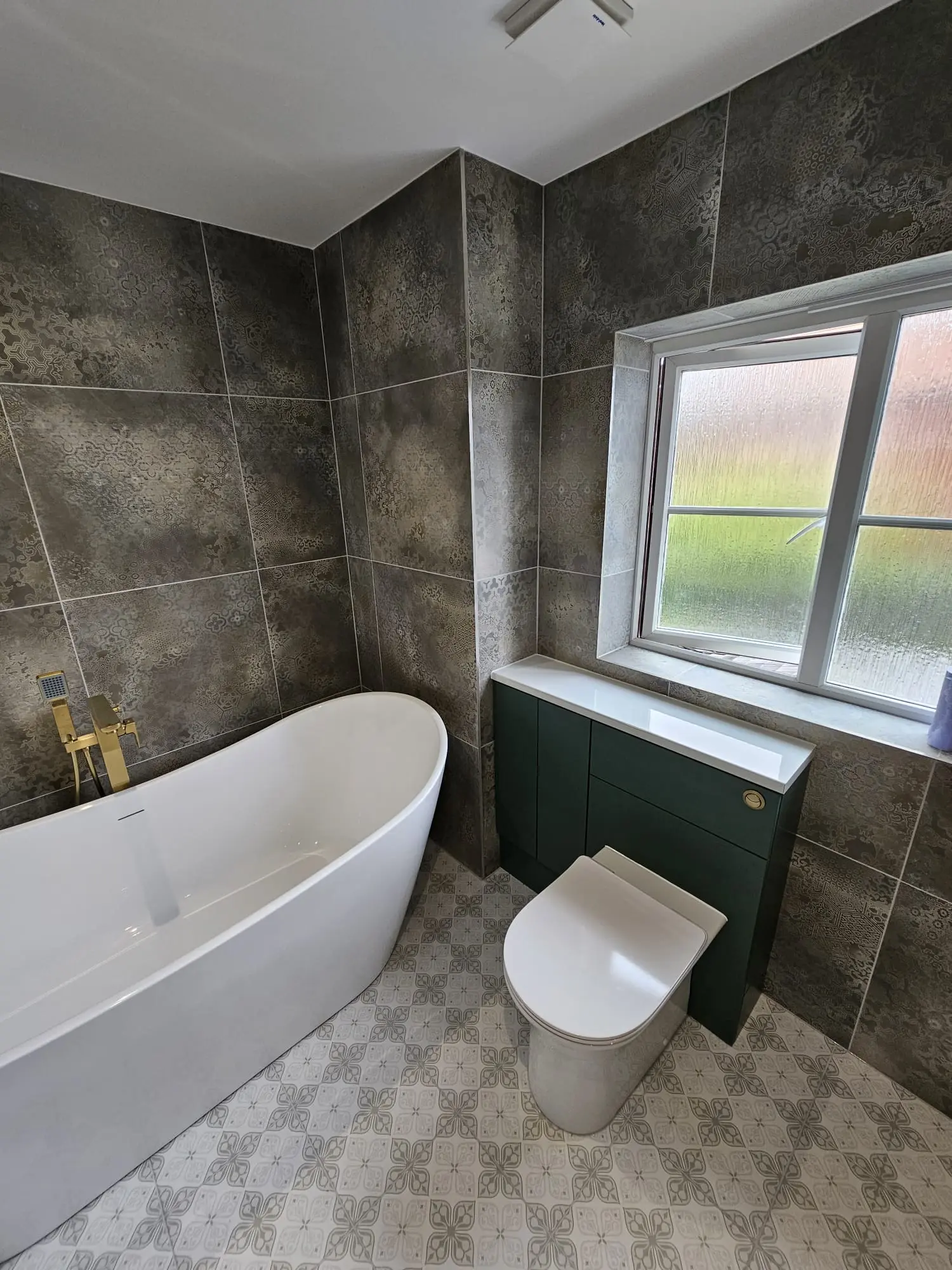 Modern bathroom with a freestanding bath, toilet and dark green vanity beneath a window